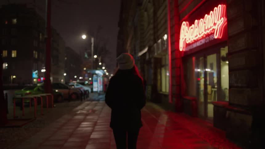 A woman walks on a city sidewalk at night