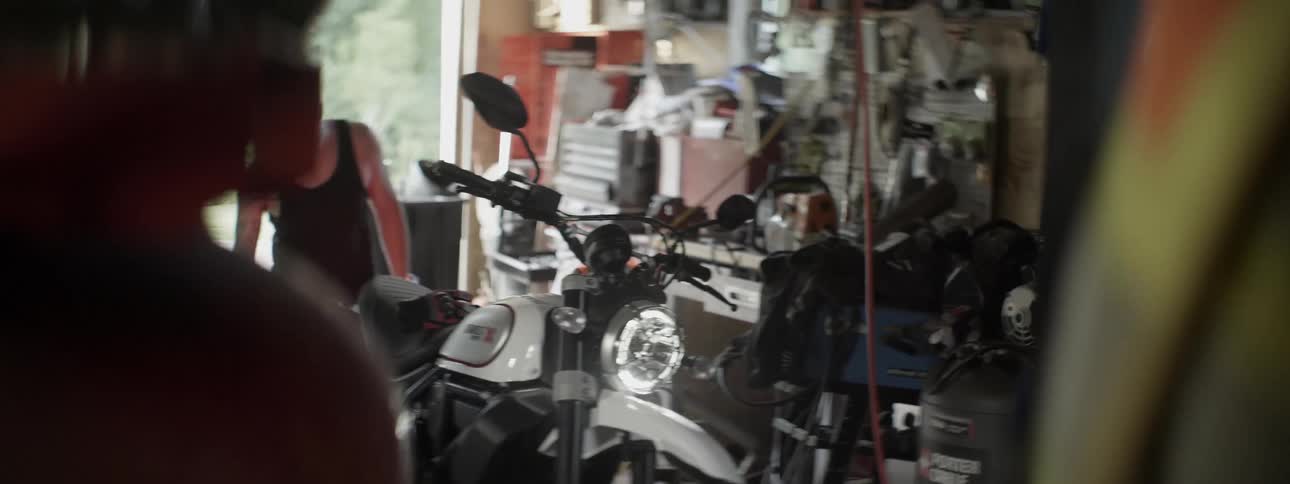 Motorcycle sits in a repair shop as a man picks up tools