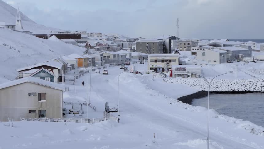 People are driving and walking in this snow covered town