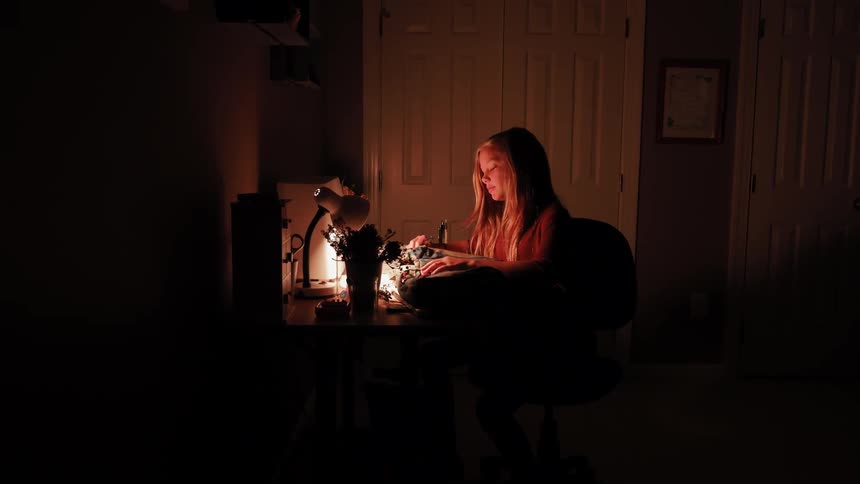 A woman sits at a desk with a lamp on