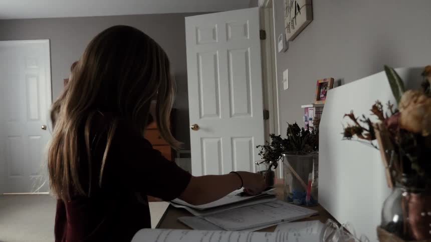 A young girl is sitting down at her desk in her room to do homework