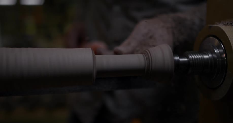 Sawdust flies as a man carves a piece of wood on a lathe