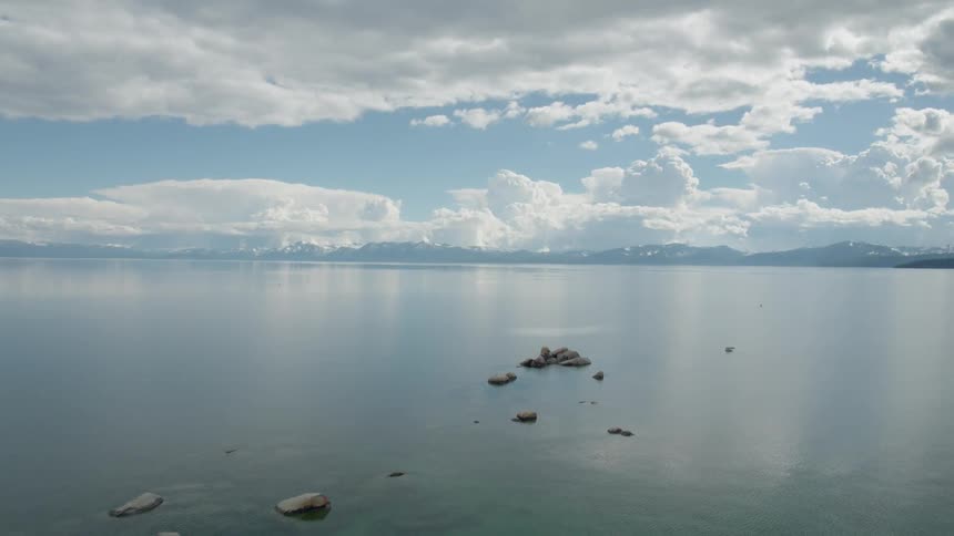 Flying over a large calm Lake Tahoe with thunder clouds in the distance