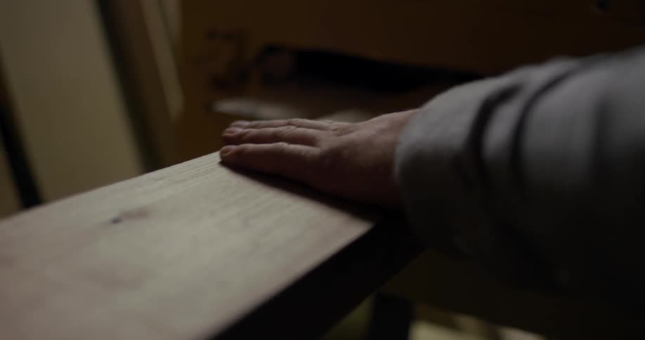 Piece of wood coming out of a machine and a person touches it