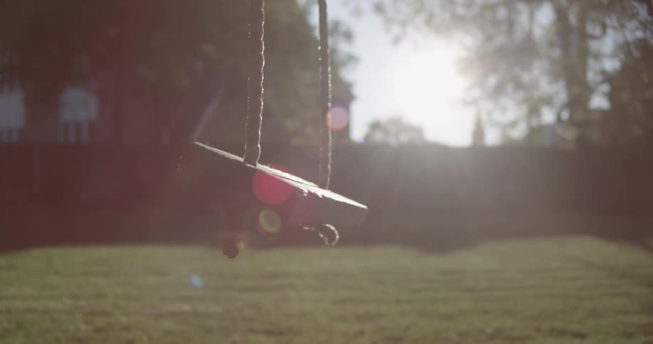 A swing slowly moves in the yard on a sunny day