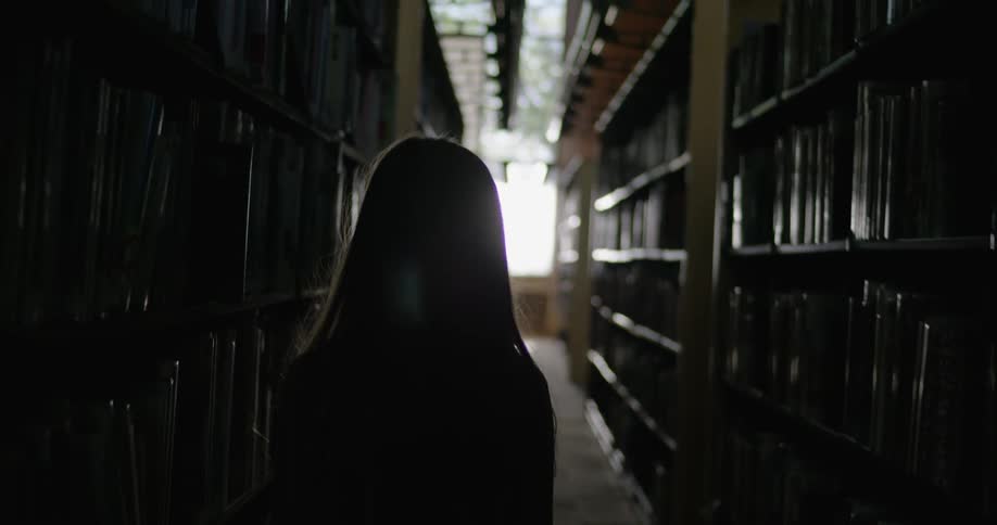 A girl is walking through a dark library