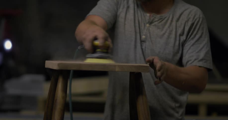A wood worker uses a sander on a piece of wood