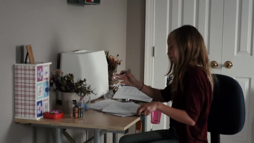 A girl drops a backpack and sits at a desk