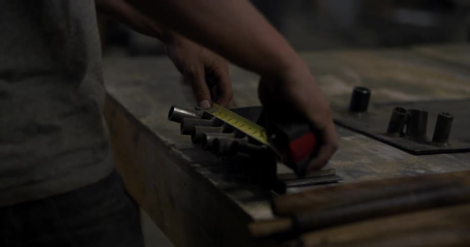 A man uses measuring tape to measure a piece of metal