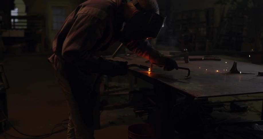 Man welds on a piece of metal in a dark shop