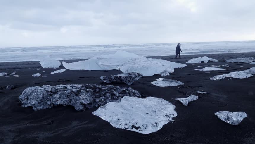 Large pieces of ice sit on a shore as people walk by