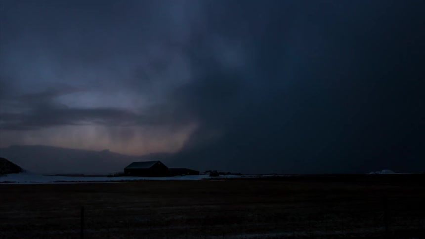 A storm rolls across a field and over a house