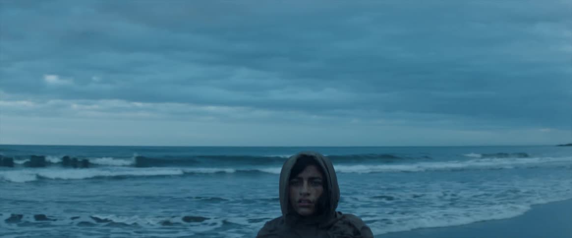A woman standing on a beach looks around