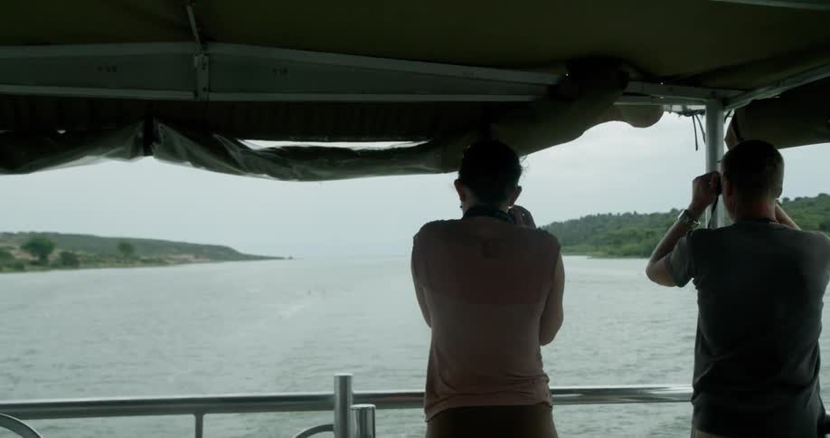 Two people watch birds flying over the water