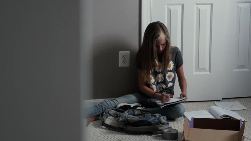 A girl sits on the floor writing in a book