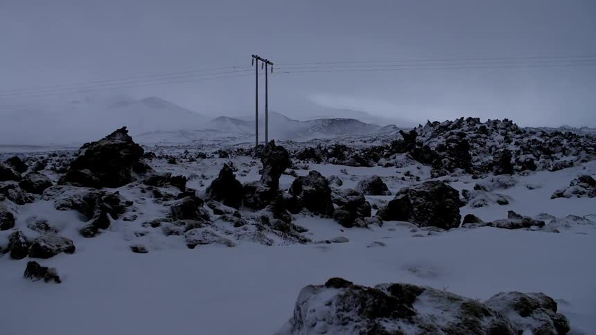 A tall power line runs through this icy rock filled field