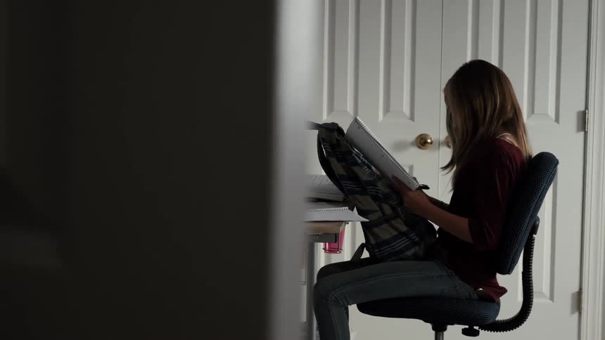 A girl does homework at a desk in her bedroom