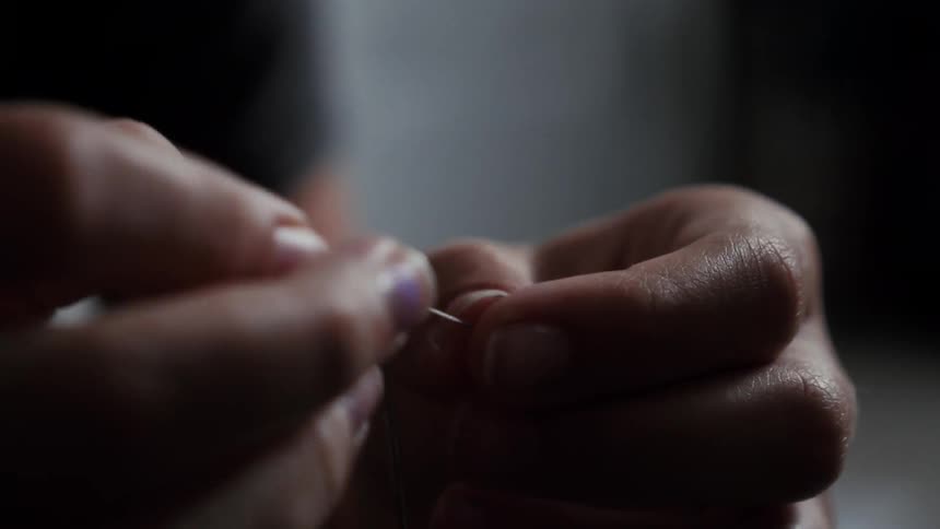 Two hands putting thread through a needle