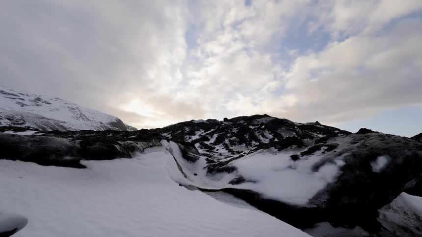 The sun filters dimly through clouds atop a snowy mountain