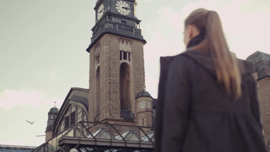A woman walks beneath a clock tower as seagulls fly around