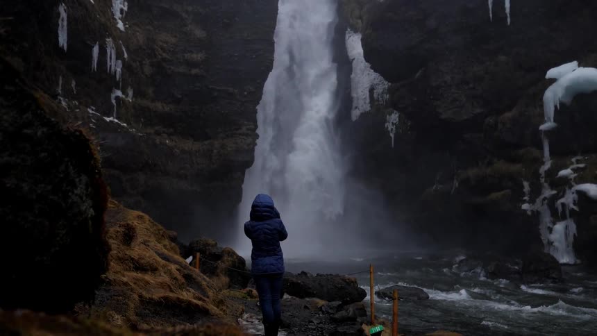 A person looks up at a snowy waterfall