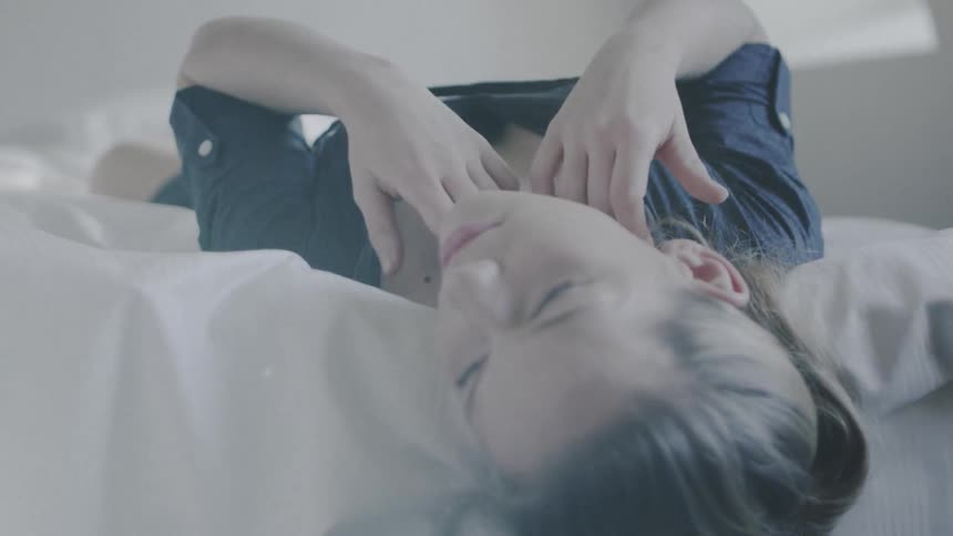Young woman lays on a bed with her head hanging over the side
