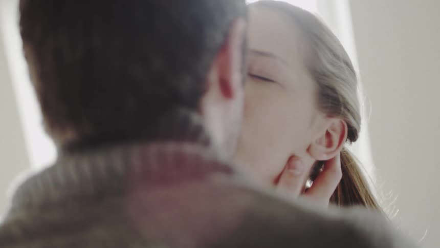 A man and woman kiss next to a sunny window