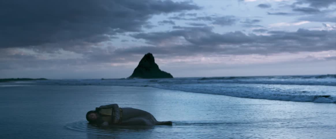 A body lays on the shore as water rolls in
