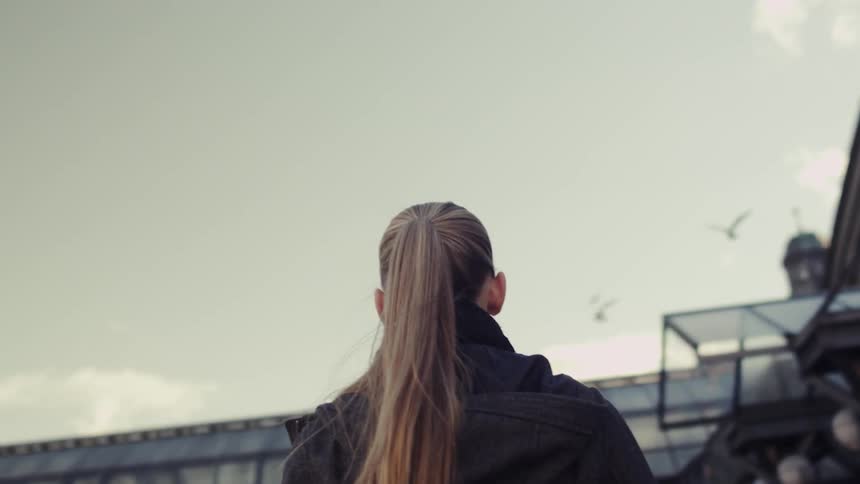 Seagulls fly above a woman in a city