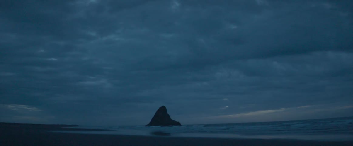 The sun is setting in the cloudy sky by the shore