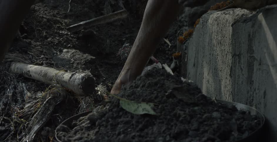 A man scoops up a pile of dirt and places it in a bowl