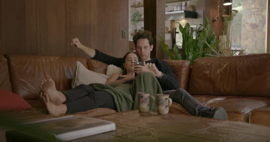 A couple sit on the couch looking a phone together