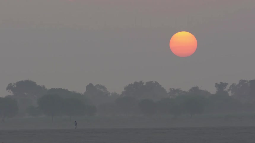 The sun glows orange in the sky as it sets over trees