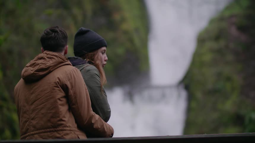 A man hugs a woman near a waterfall