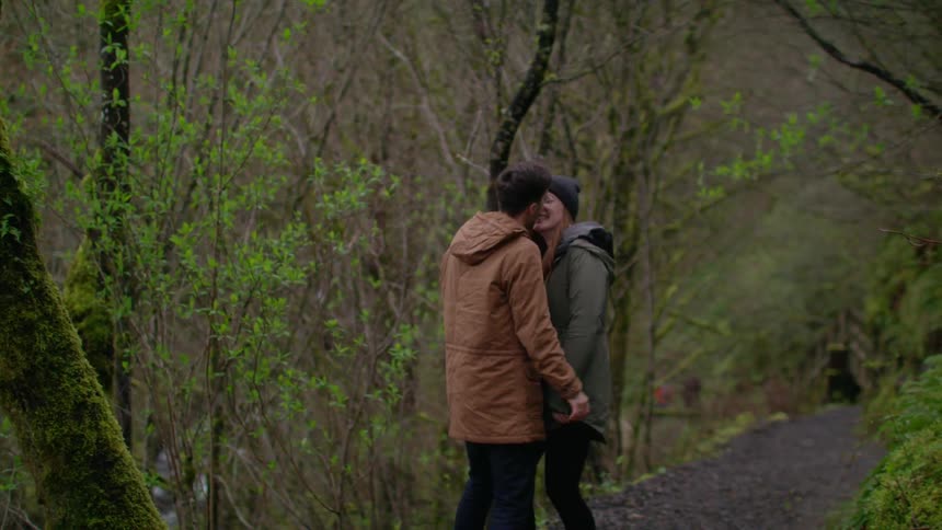 A man and woman kiss while hiking in the woods
