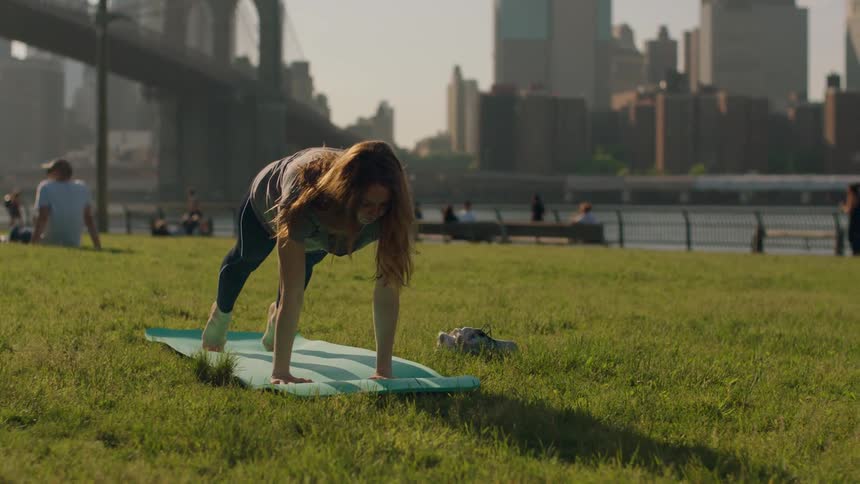 A woman stretches and does yoga poses in a city park during the day
