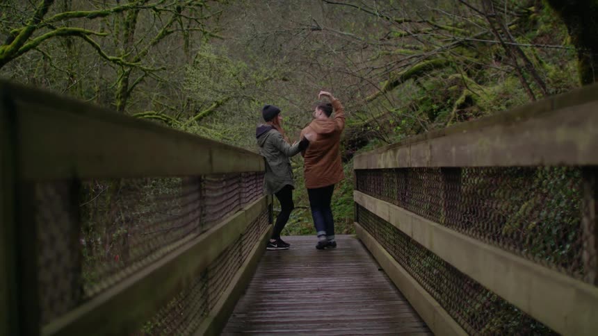 A man and woman dance on a wood bridge