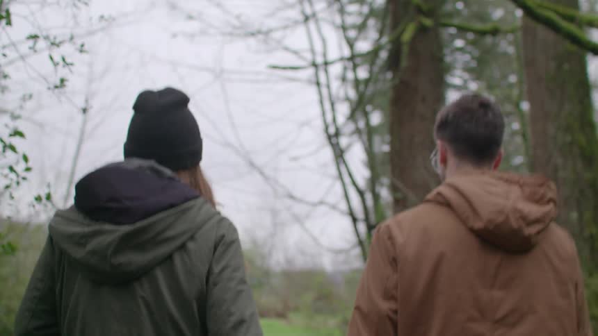 Man and woman walk hand in hand through the woods