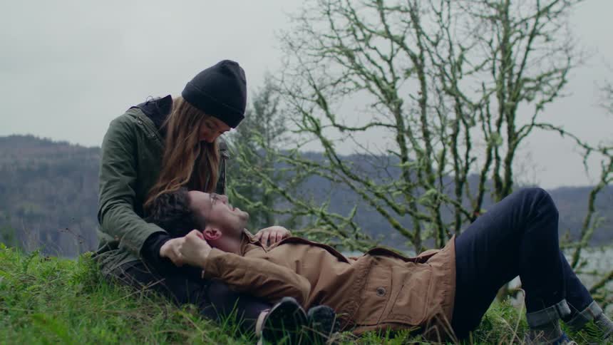 A man lays down on a woman's lap on a grassy hillside