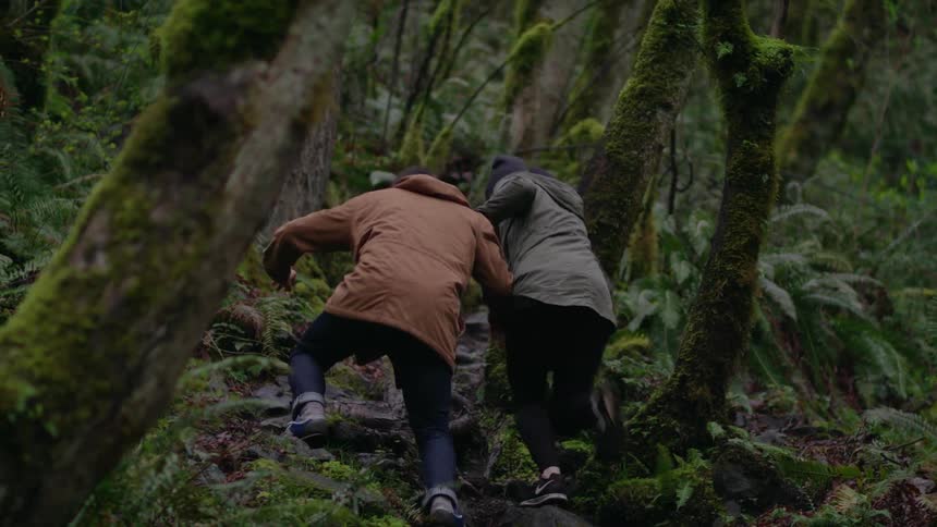 A man and woman hold hands while hiking in the woods and start to race up a hillside