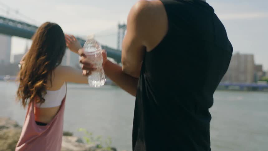 A man and woman stretch by the water