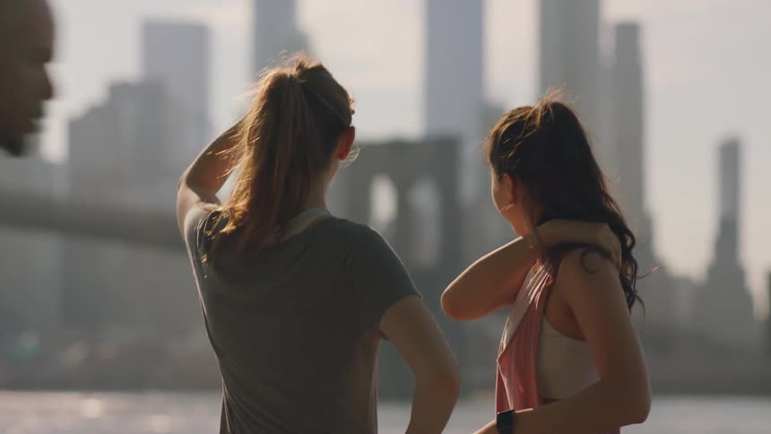 Two women stretch and talk in a city during the day
