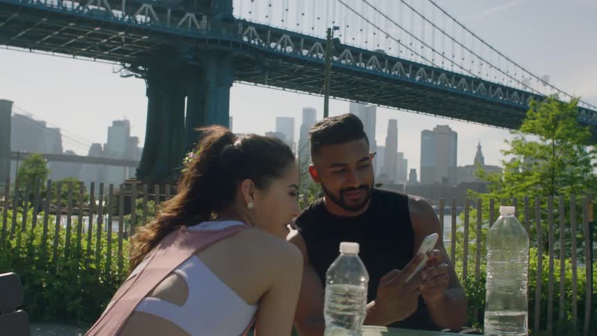 A man and woman drink from water bottles and look at a phone in a city park