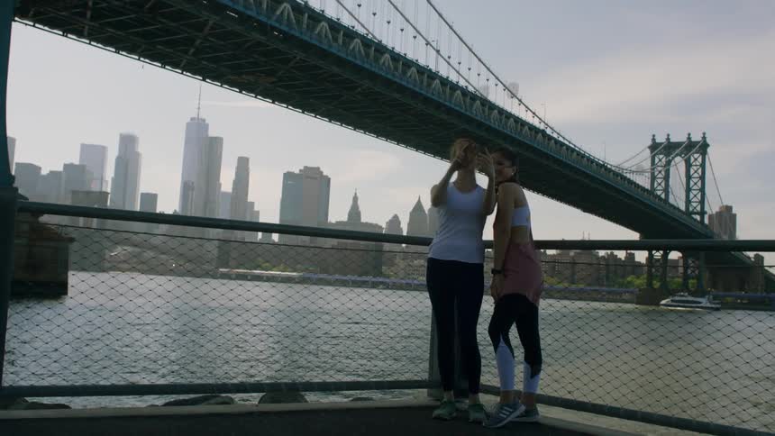 Two women joggers take a picture by a bridge