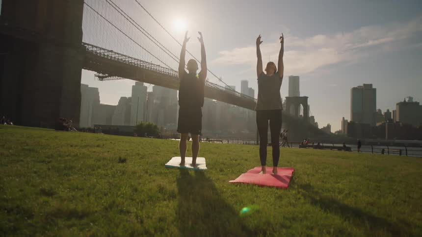A man and woman do yoga out in a city park