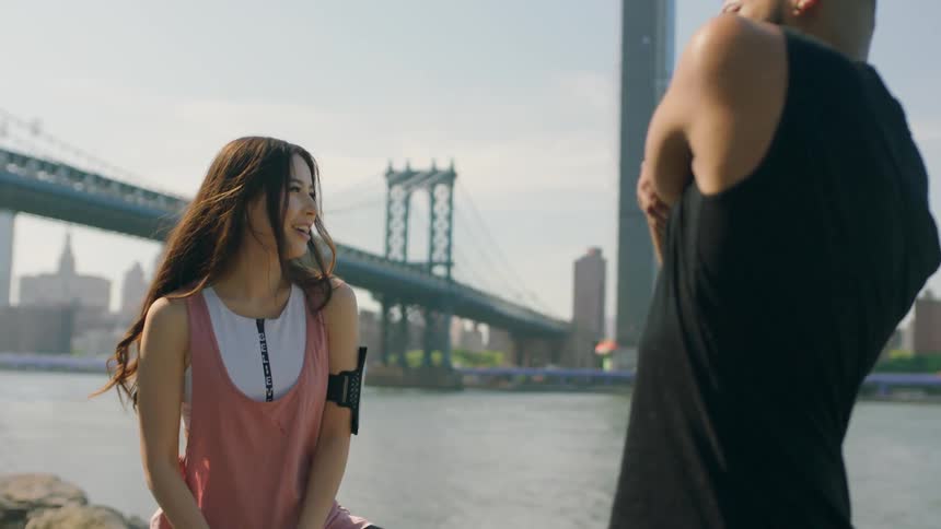 A man and woman stretch their muscles near a city bridge