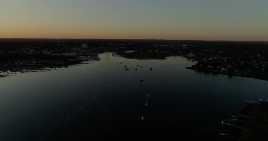 A group of boats in the water is being filmed by a drone at sunset
