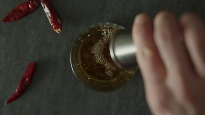 Liquid being poured into a glass with three chili peppers on the table