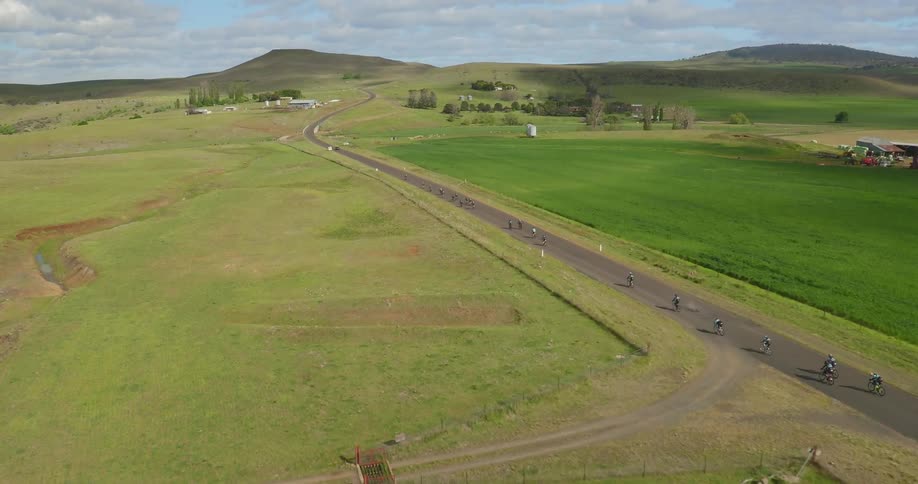 Bicycle riders race down a long road on a cloudy day