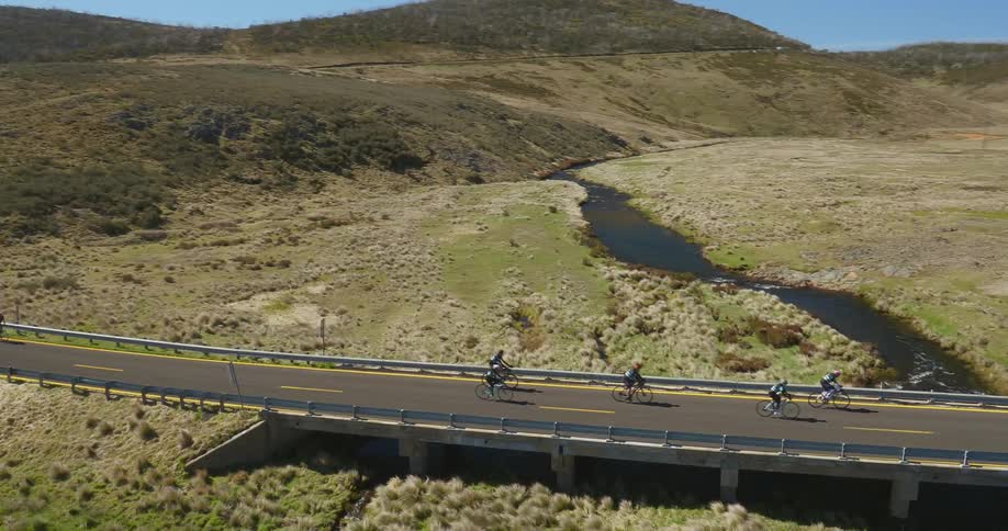 People are racing on bicycles across a road going over a stream